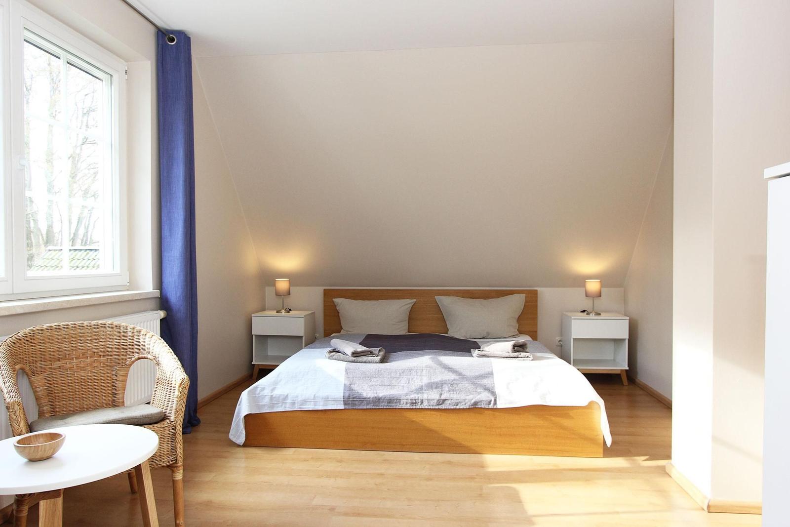Schlafzimmer mit Doppelbett, zwei Nachttischen und Fenster mit blauen Vorhängen.