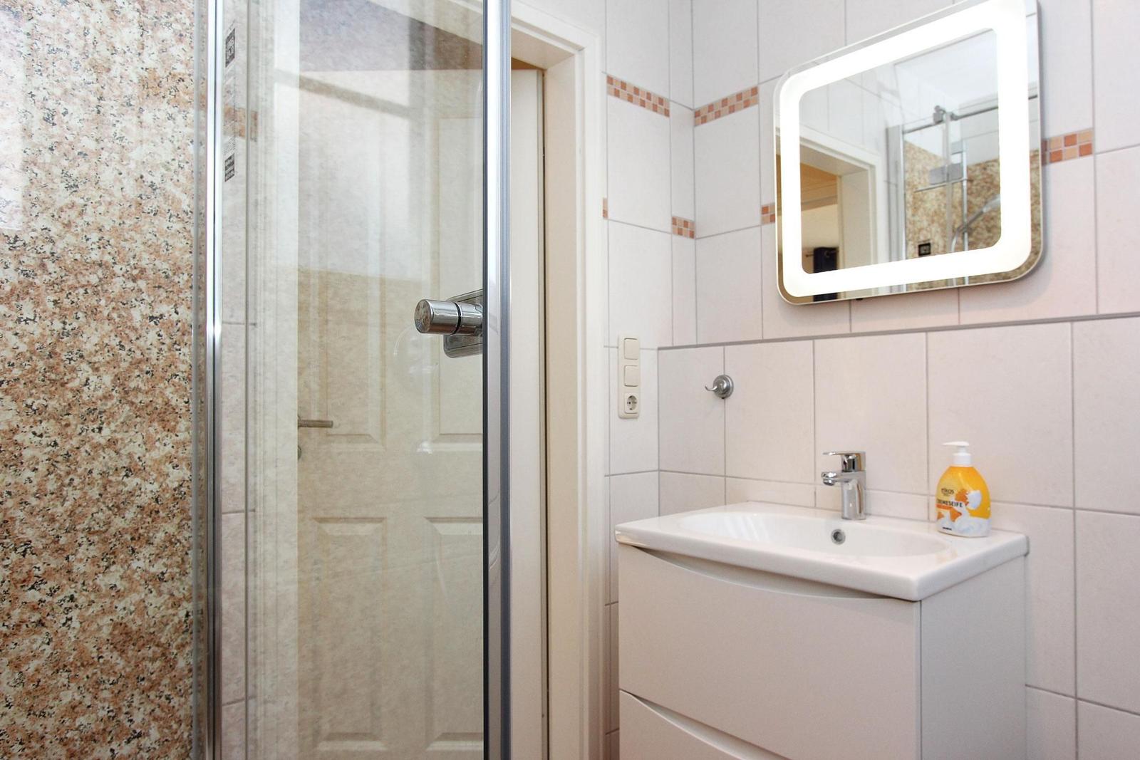 Badezimmer mit Dusche, Waschbecken und beleuchtetem Spiegel