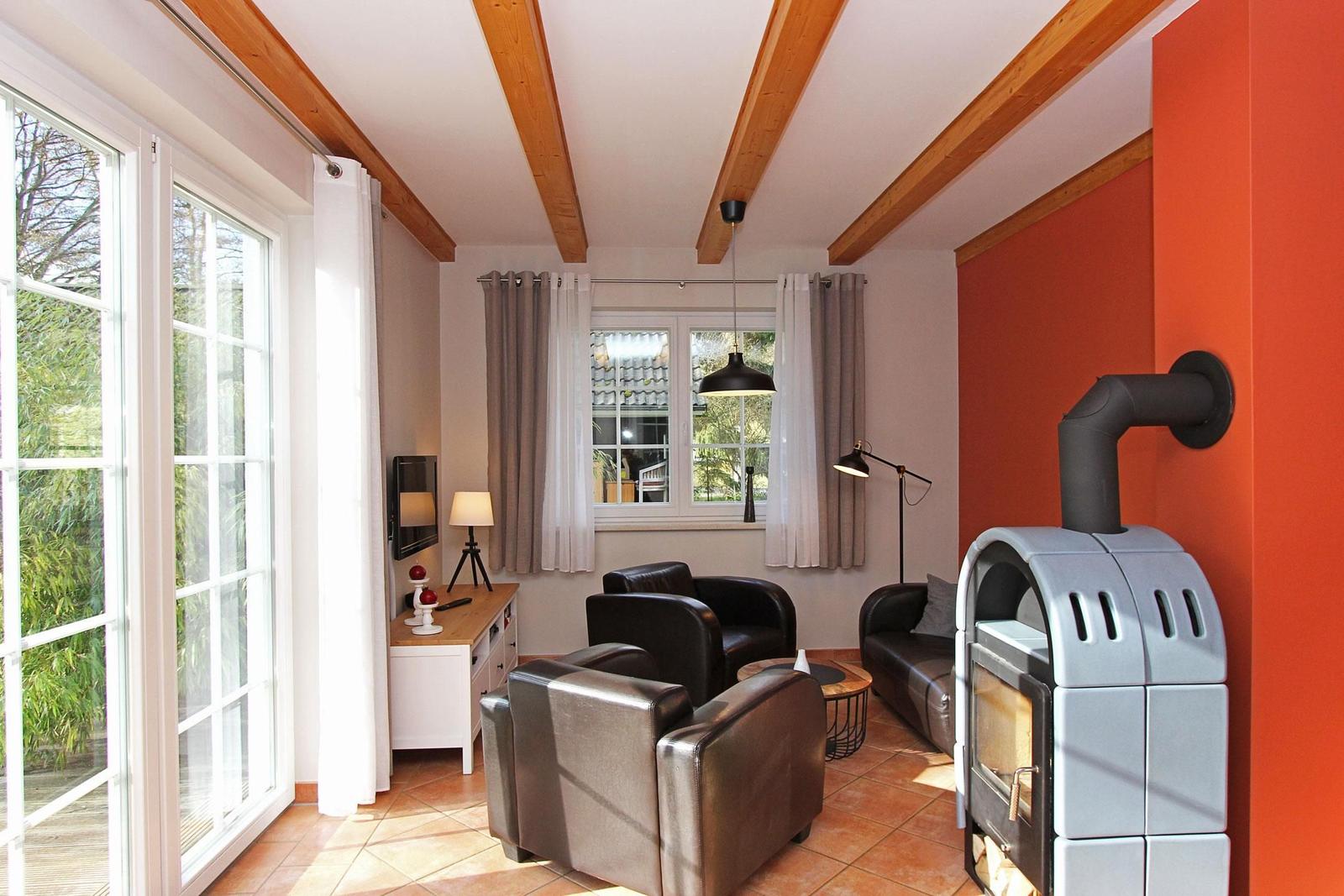 Wohnzimmer mit Holzbalken, roter Wand, Kaminofen und Sitzgelegenheiten.