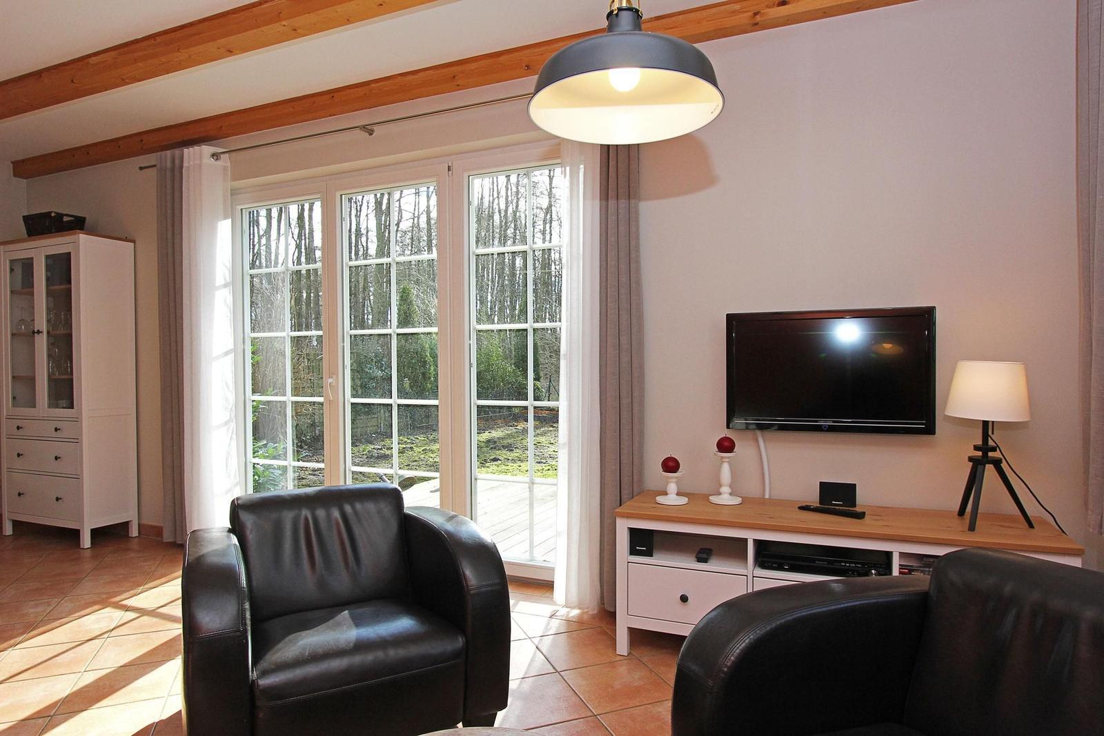 Wohnzimmer mit zwei schwarzen Ledersesseln, TV, Schrank und Fenster zum Garten.