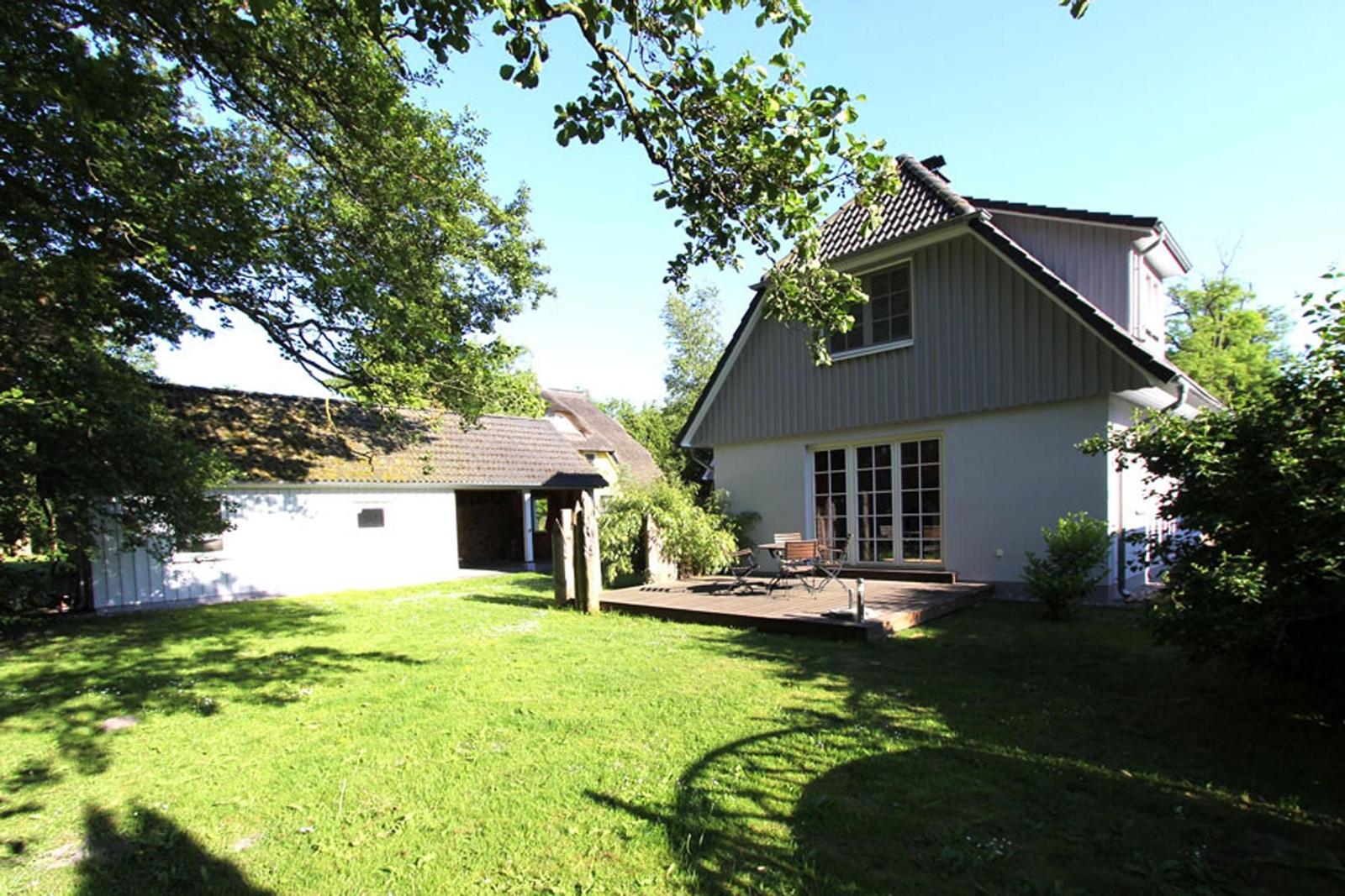 Haus mit Terrasse, Garten und Bäumen unter blauem Himmel.