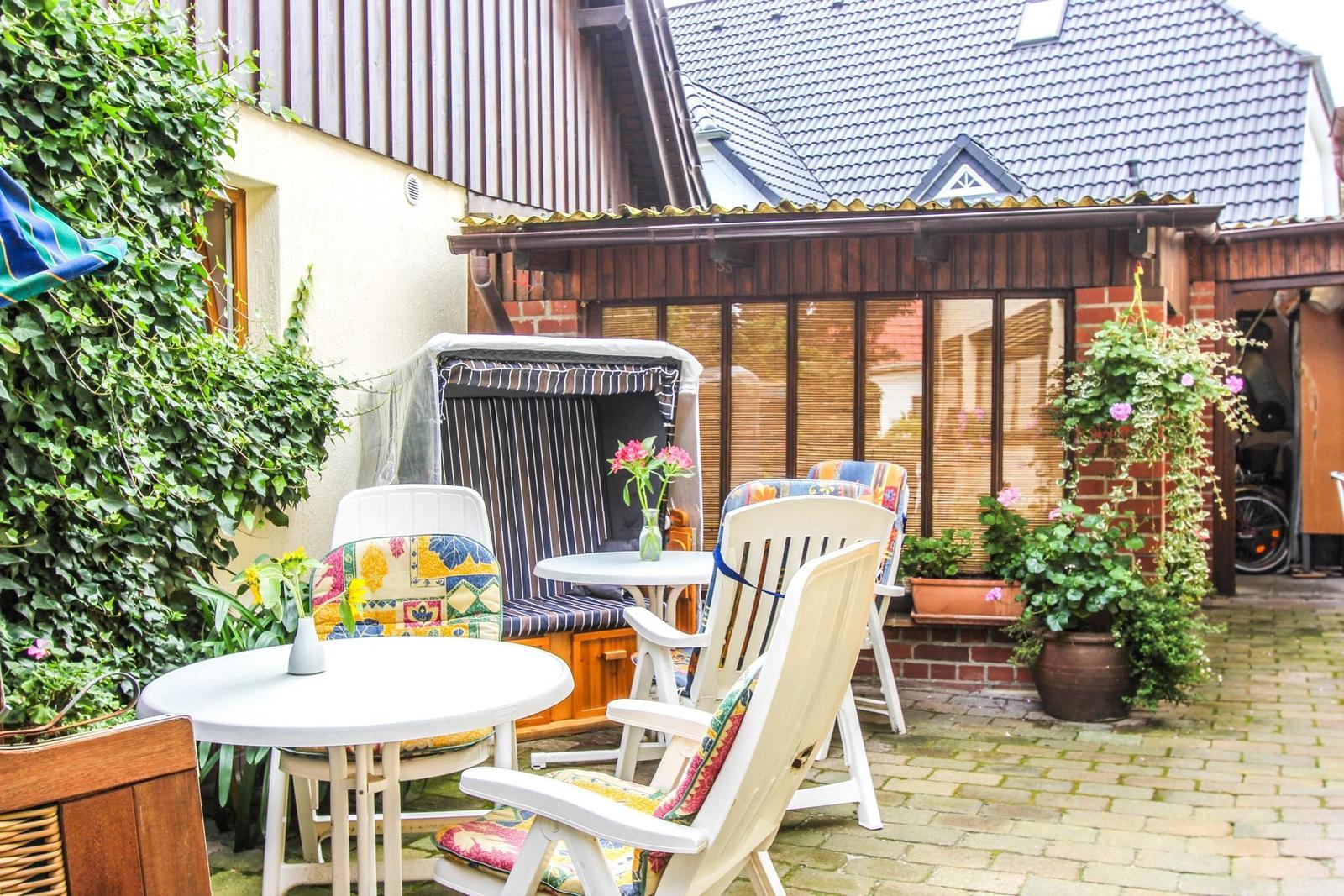 Terrasse mit Tischen, Stühlen und Pflanzen. Hinterhof mit Holzhaus und Kletterpflanzen.