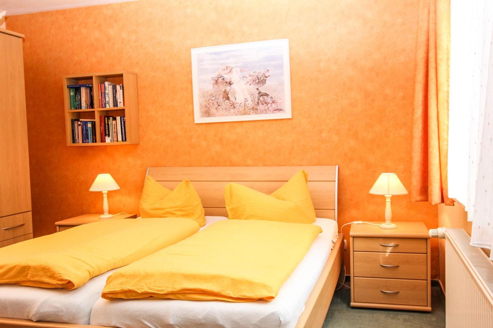 Schlafzimmer mit Doppelbett, Nachttischen und Wandbild. Wandfarbe orange.