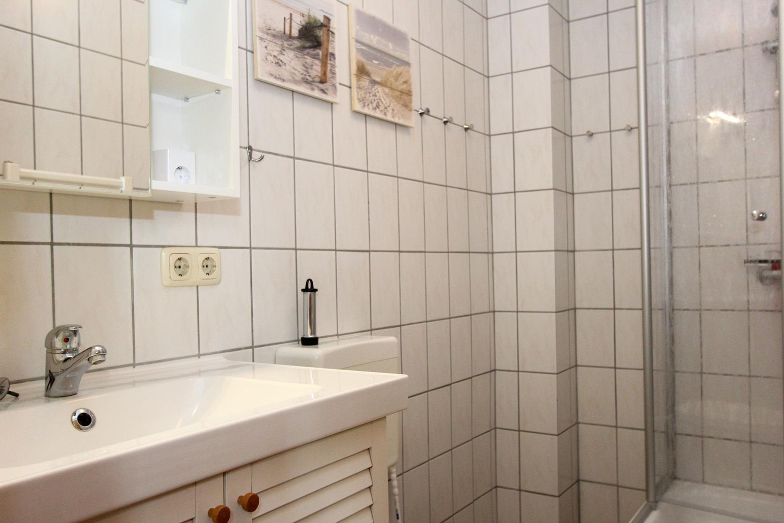 Badezimmer mit Waschbecken, Dusche und Wandbildern.