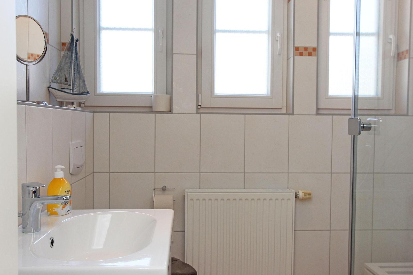 Badezimmer mit Waschbecken, Dusche und Fenstern.