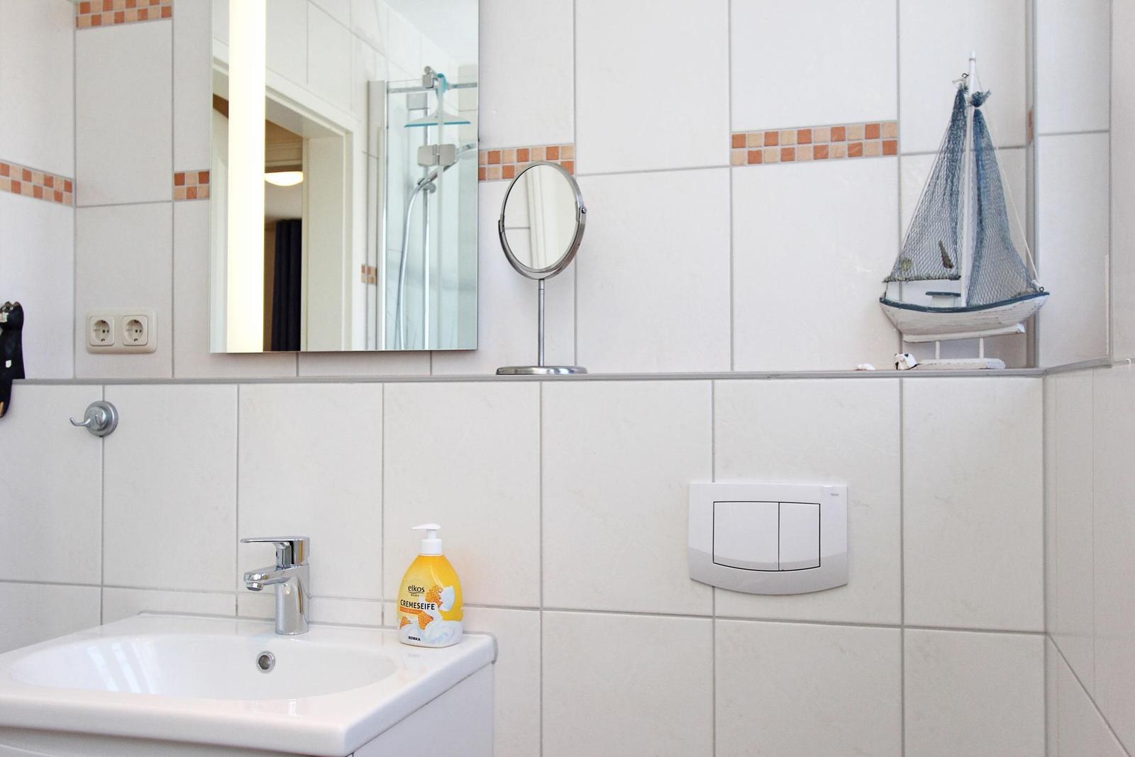 Badezimmer mit Waschbecken, Spiegel und Segelschiffmodell auf der Arbeitsplatte.