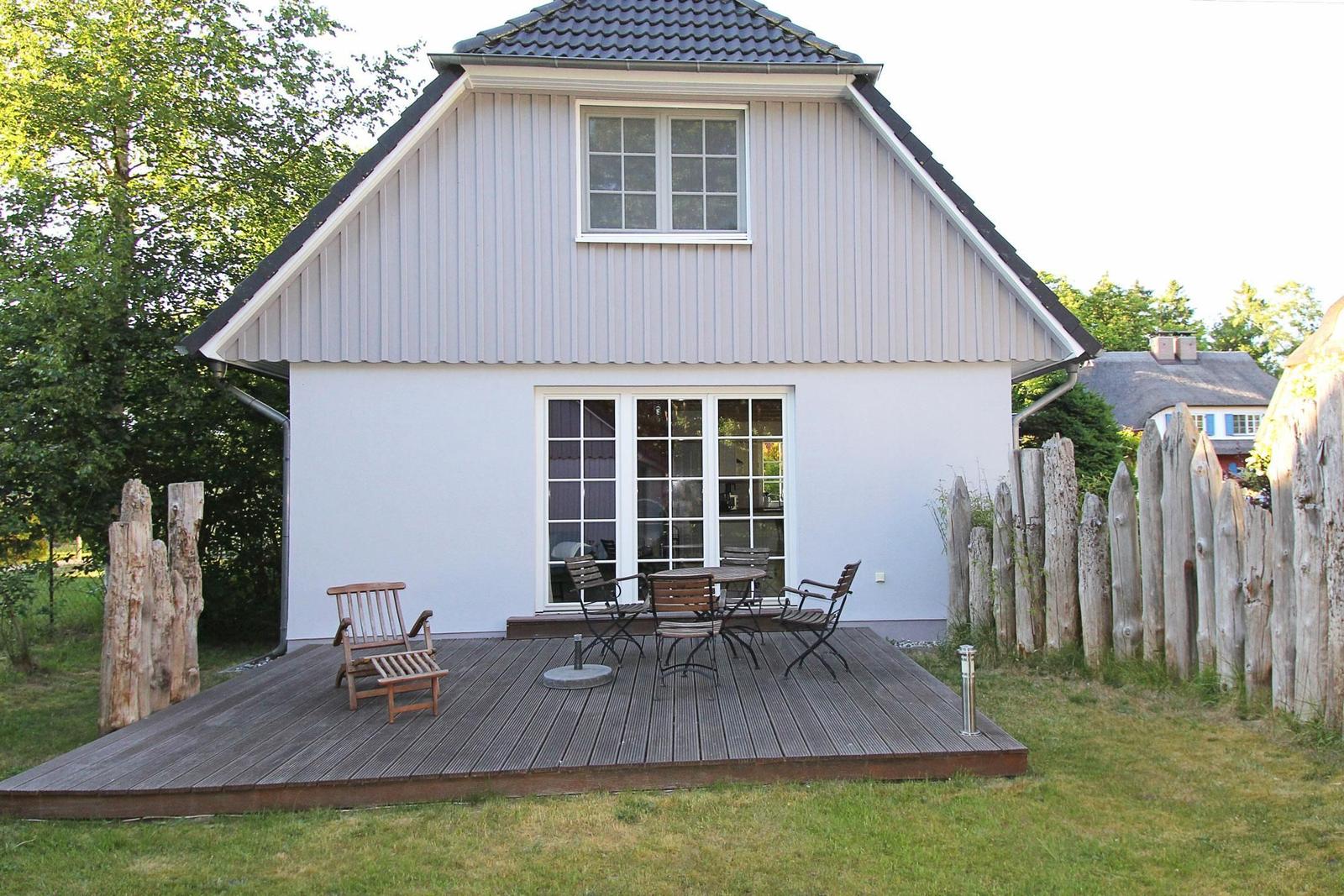 Haus mit Terrasse, Garten und Holzgeländer. Tisch und Stühle auf der Terrasse.