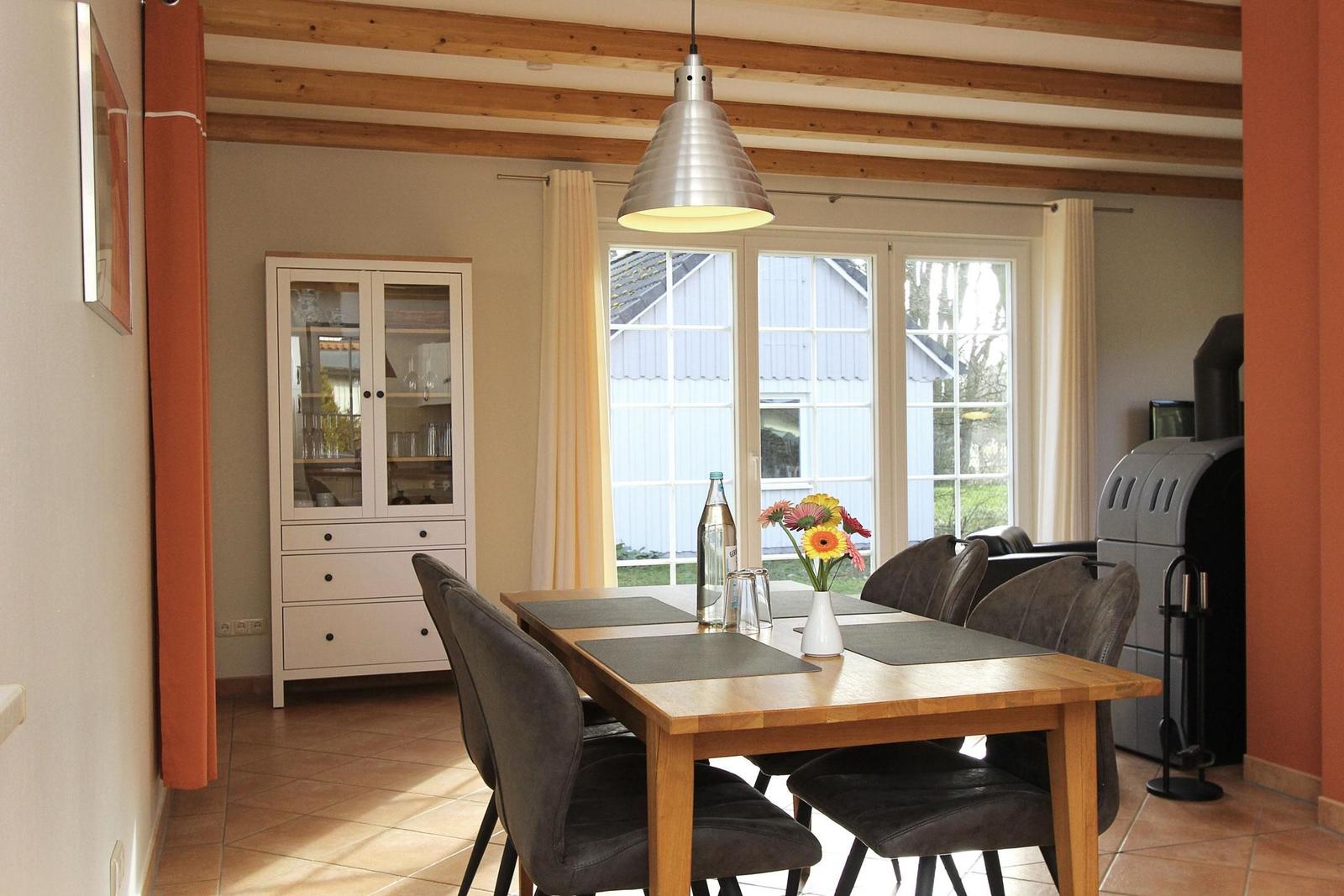 Esszimmer mit Holztisch, Stühlen und Glasvitrine. Fenster mit Blick auf Haus.