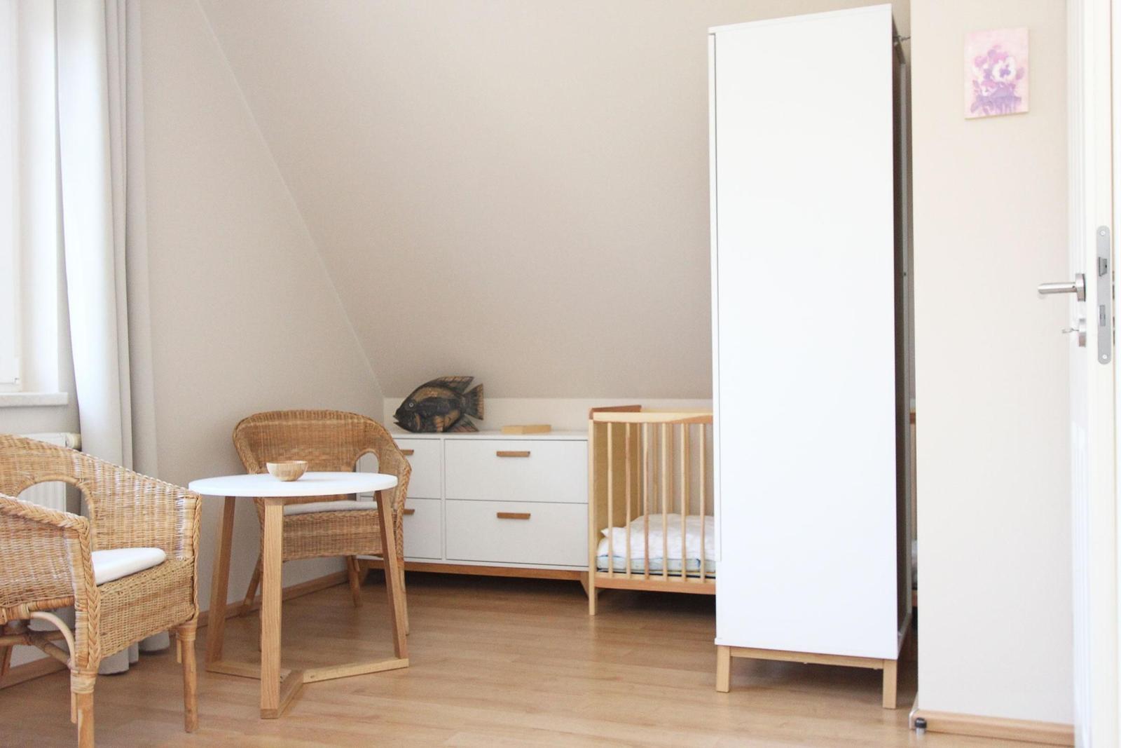 Kinderzimmer mit Babybett, Schrank und Esstisch mit Stühlen.