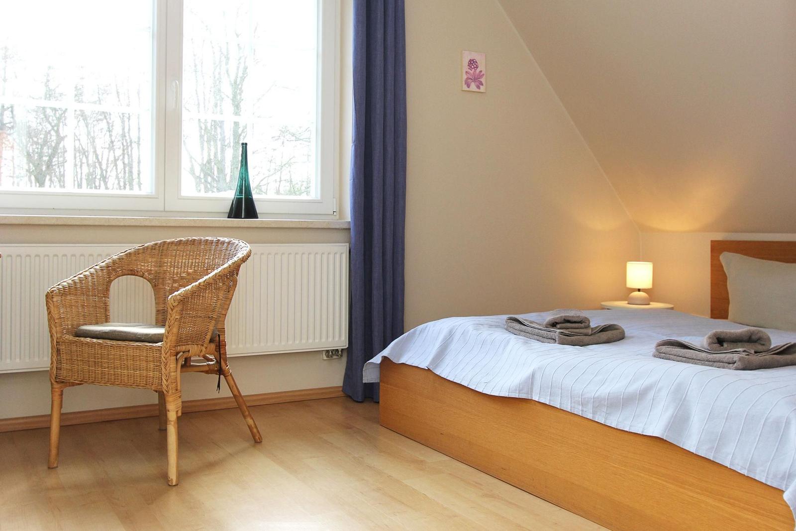 Schlafzimmer mit Bett, Stuhl und Fenster. Holzboden und Wand mit Dachneigung.