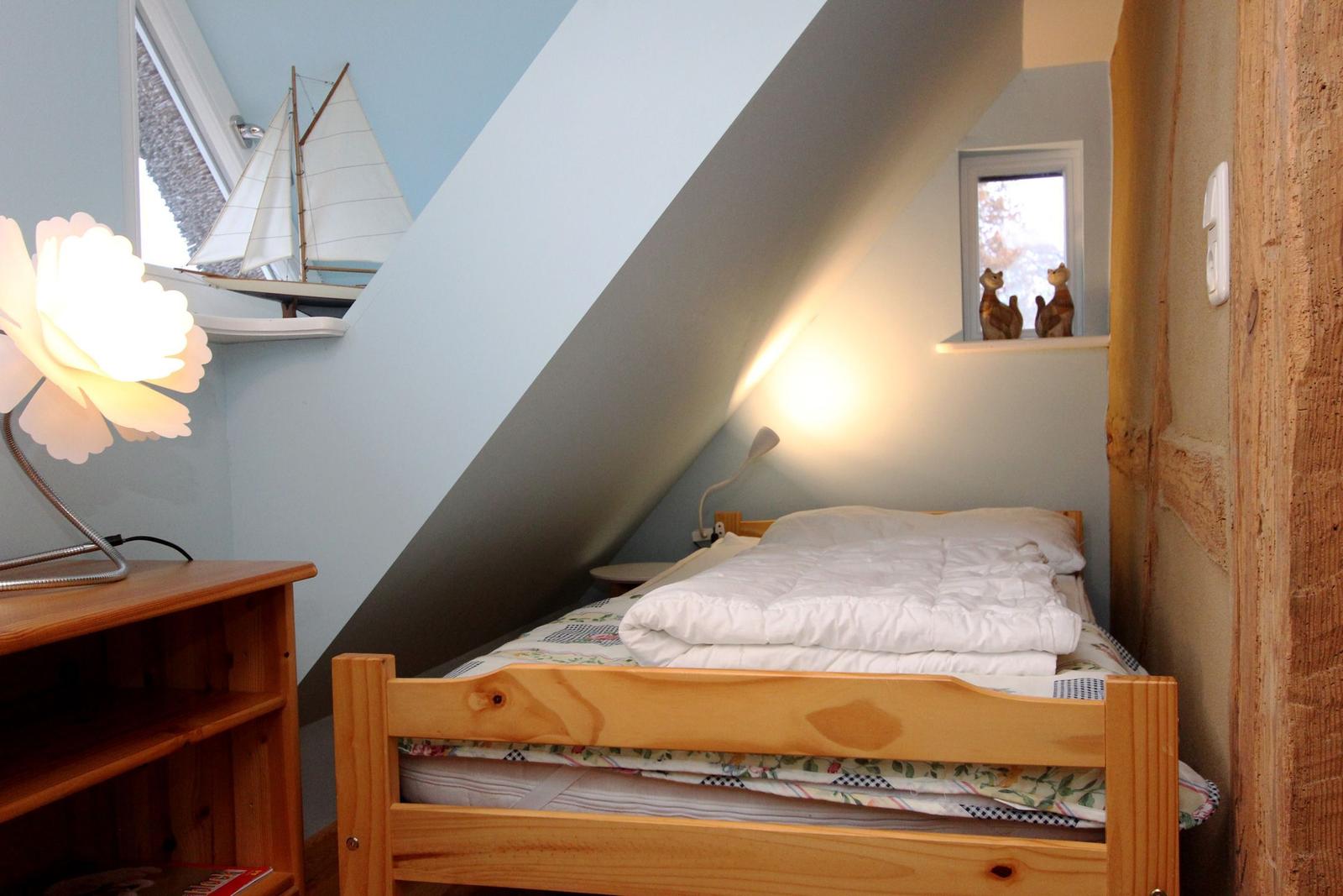 Schlafzimmer mit Holzbett, Nachttisch und Fenster. Wandgestaltung mit Segelschiffmodell.