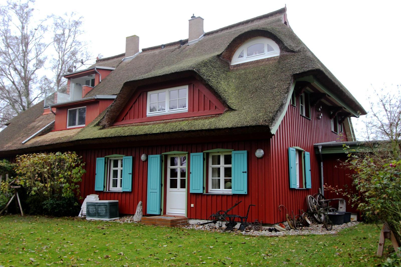 Rotes Haus mit Strohdach, blauen Fensterläden und grünem Garten.