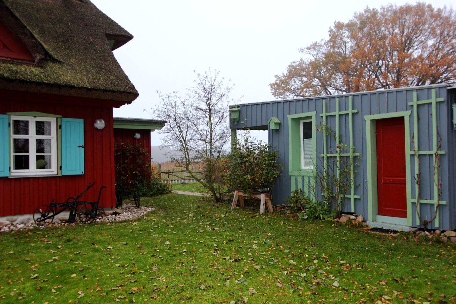Rotes und blaues Gebäude mit grünen Fensterrahmen und roter Tür im Garten.