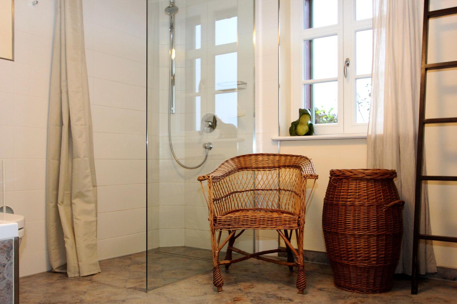 Bad mit Dusche, Bambusstuhl und Korb neben Fenster