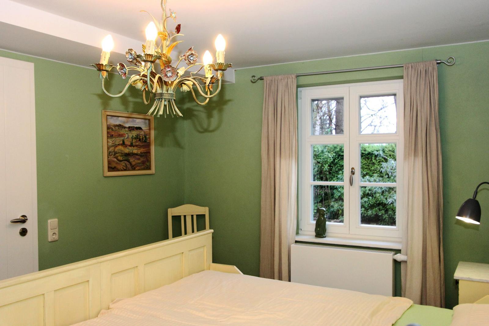 Schlafzimmer mit grüner Wand, Bett, Fenster und Kronleuchter.