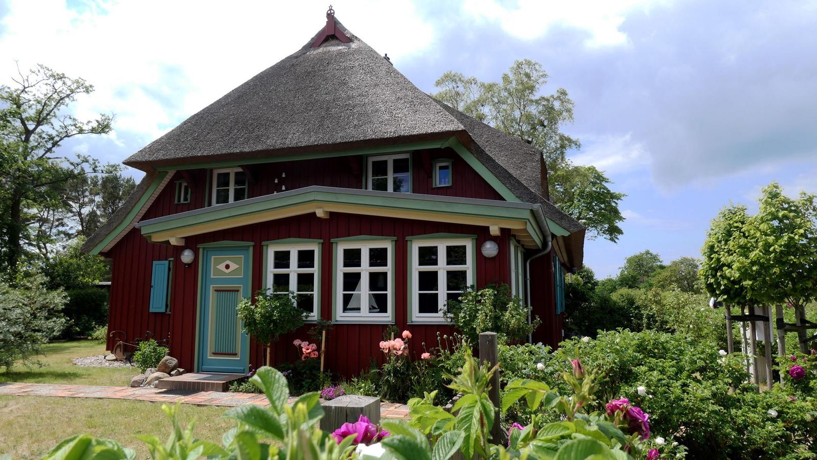 Rotes Haus mit Strohdach und blauer Tür im Garten mit Blumen.