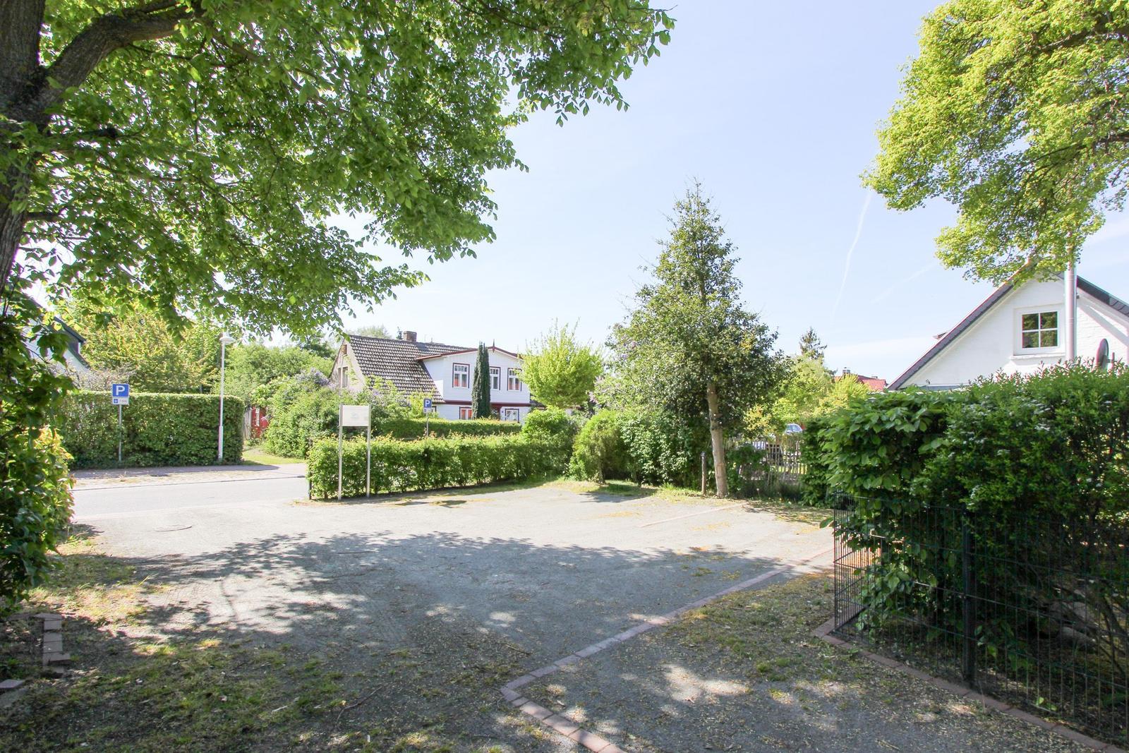 Haus mit gepflegtem Garten und Parkplatz unter Bäumen.