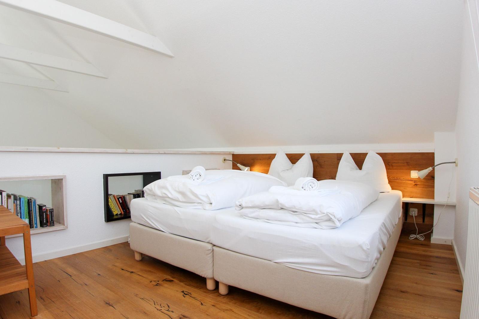 Zimmer mit Doppelbett, Holzboden und Dachschräge. Bücherregale an der Wand.