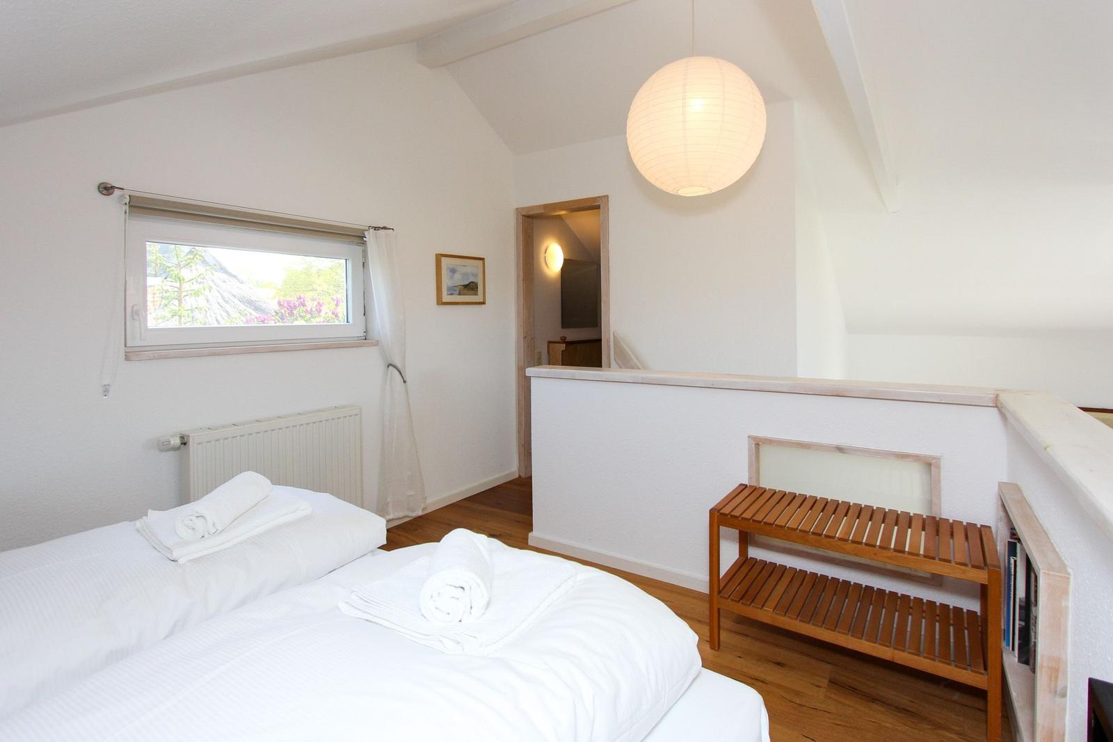 Schlafzimmer mit Bett, Fenster und Holzbank. Decke mit Balken und Pendelleuchte.