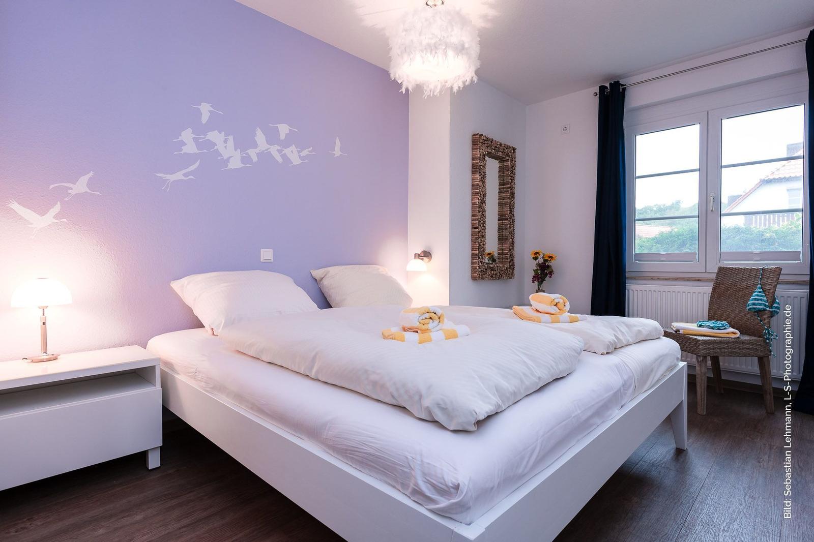 Schlafzimmer mit Bett, Nachttisch, Fenster und Wanddekoration.