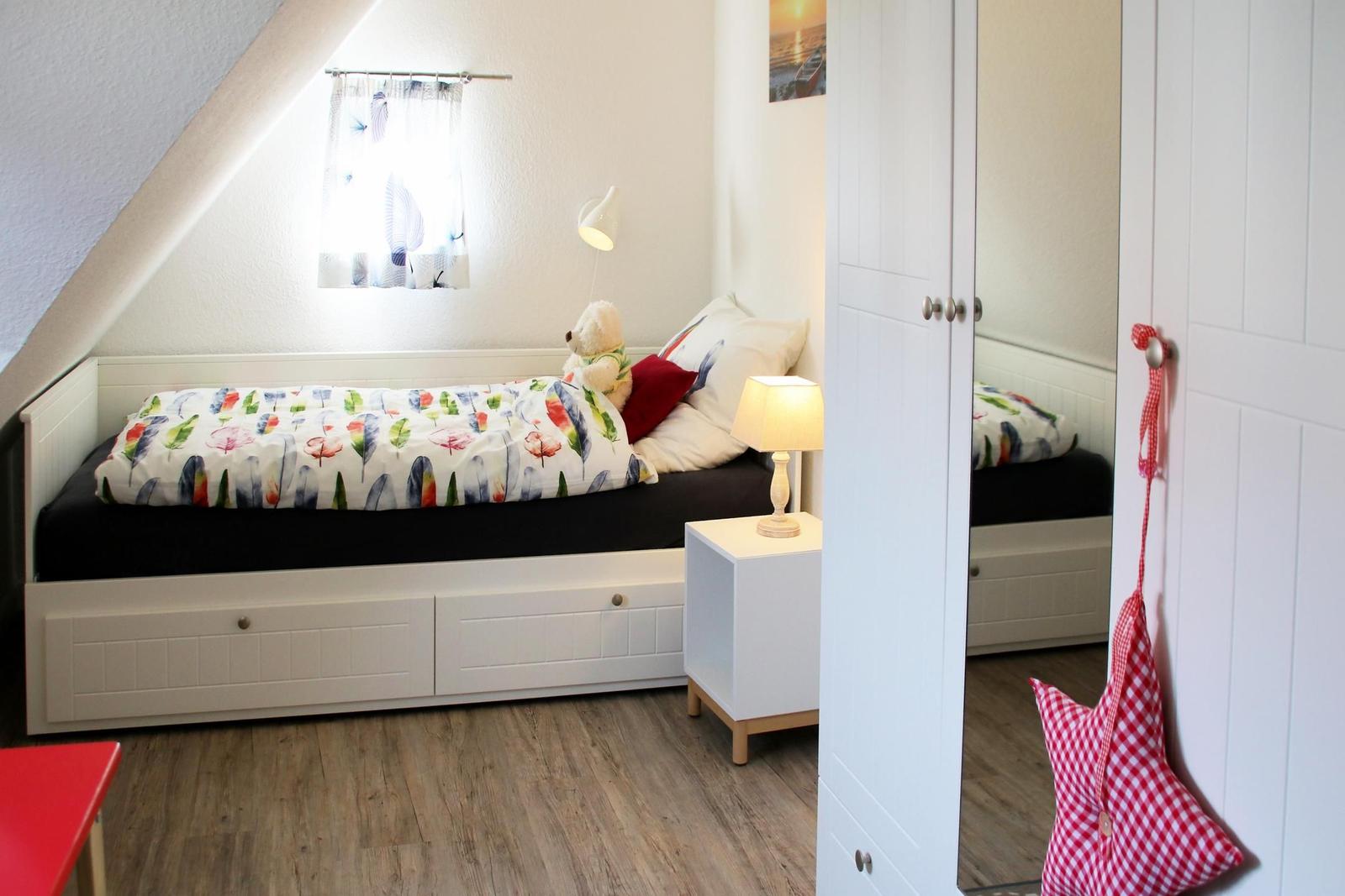 Ein Schlafzimmer mit Dachschrägen, weißem Bett und Nachttisch mit Lampe.