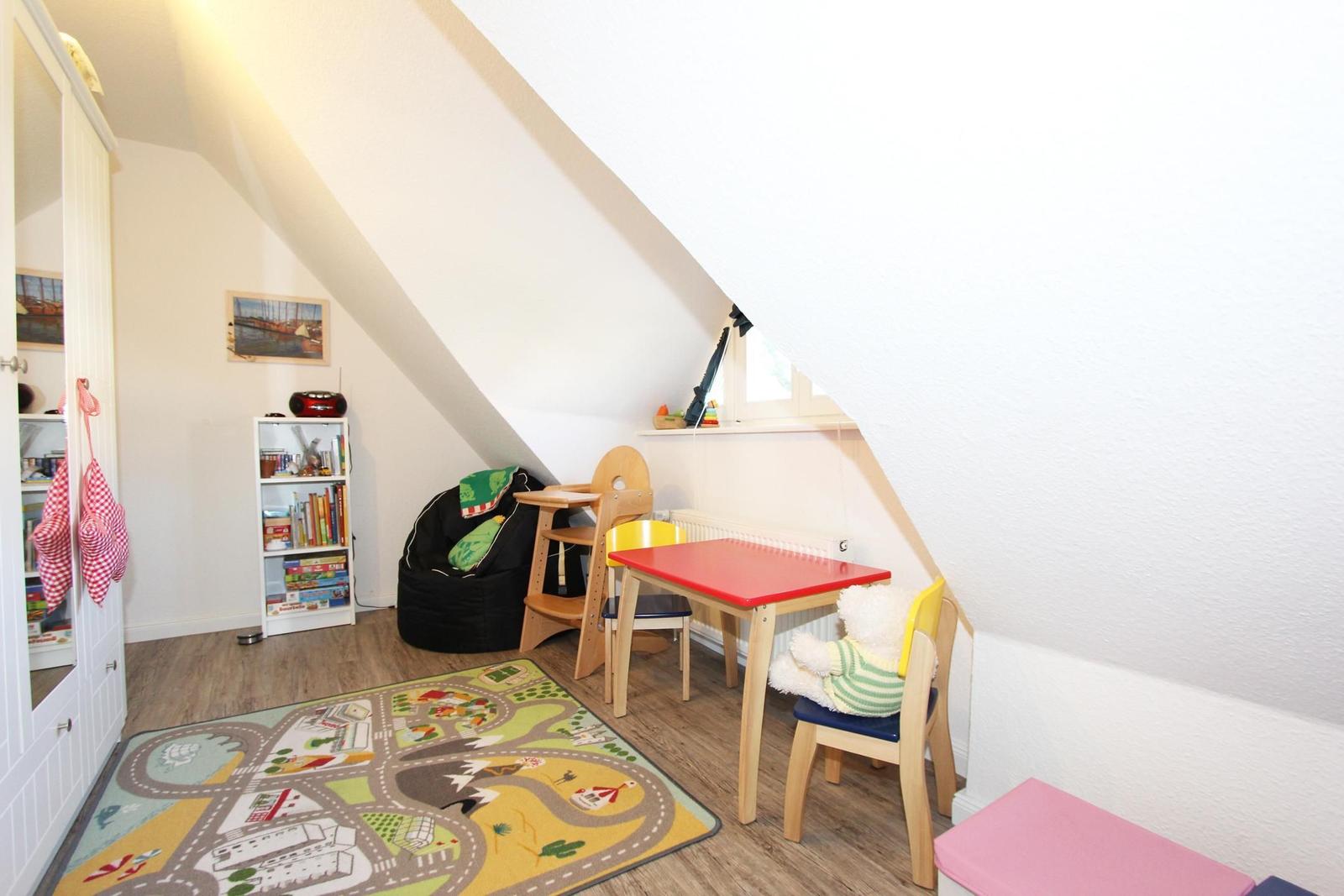 Kinderzimmer mit Spielzeug, Tisch, Stühlen und Teppich unter schrägen Dachschrägen.