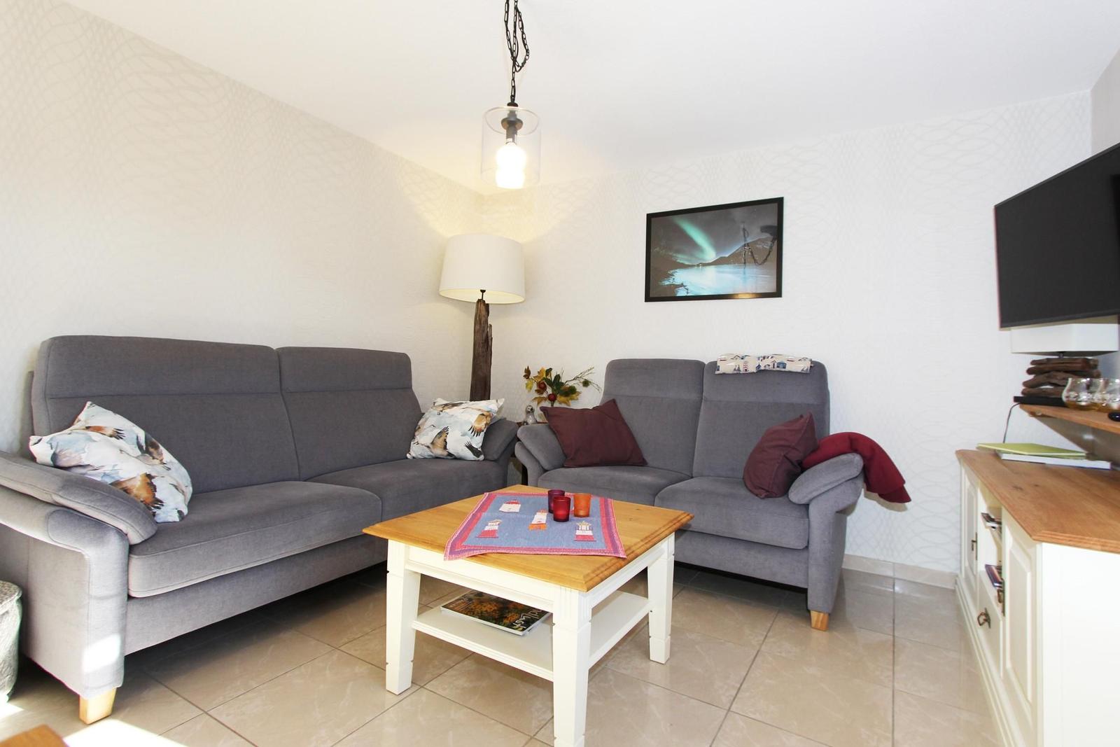 Wohnzimmer mit grauem Sofa, Couchtisch und Fernseher.