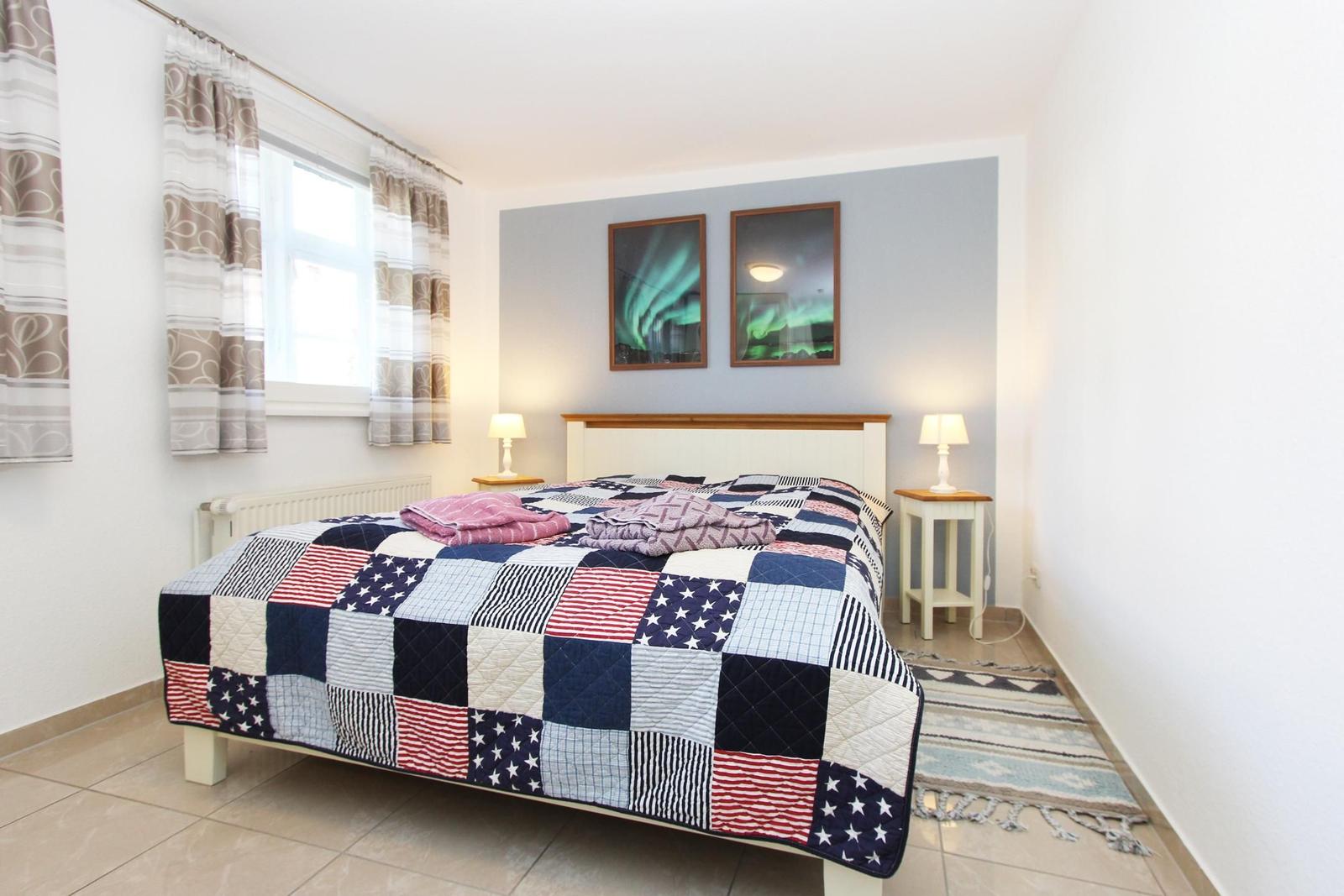 Schlafzimmer mit Bett, Fenster und zwei Nachttischen mit Lampen.
