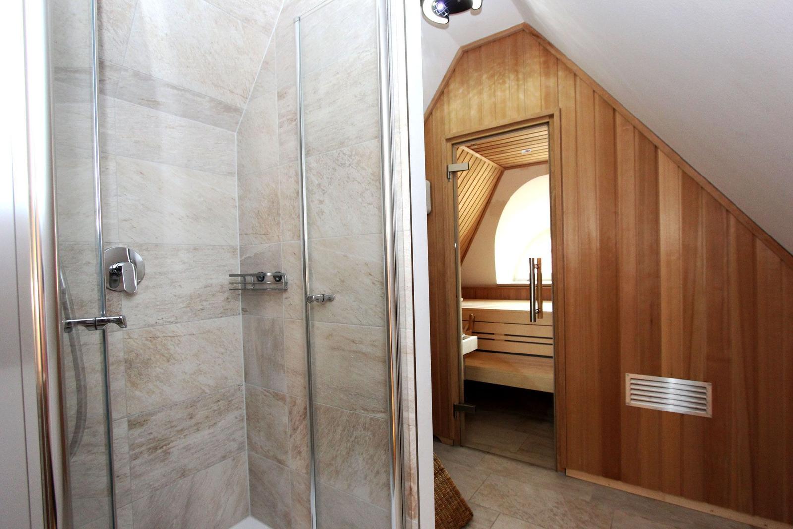 Dusche mit Glaswand und Holzsauna mit Sitzbank