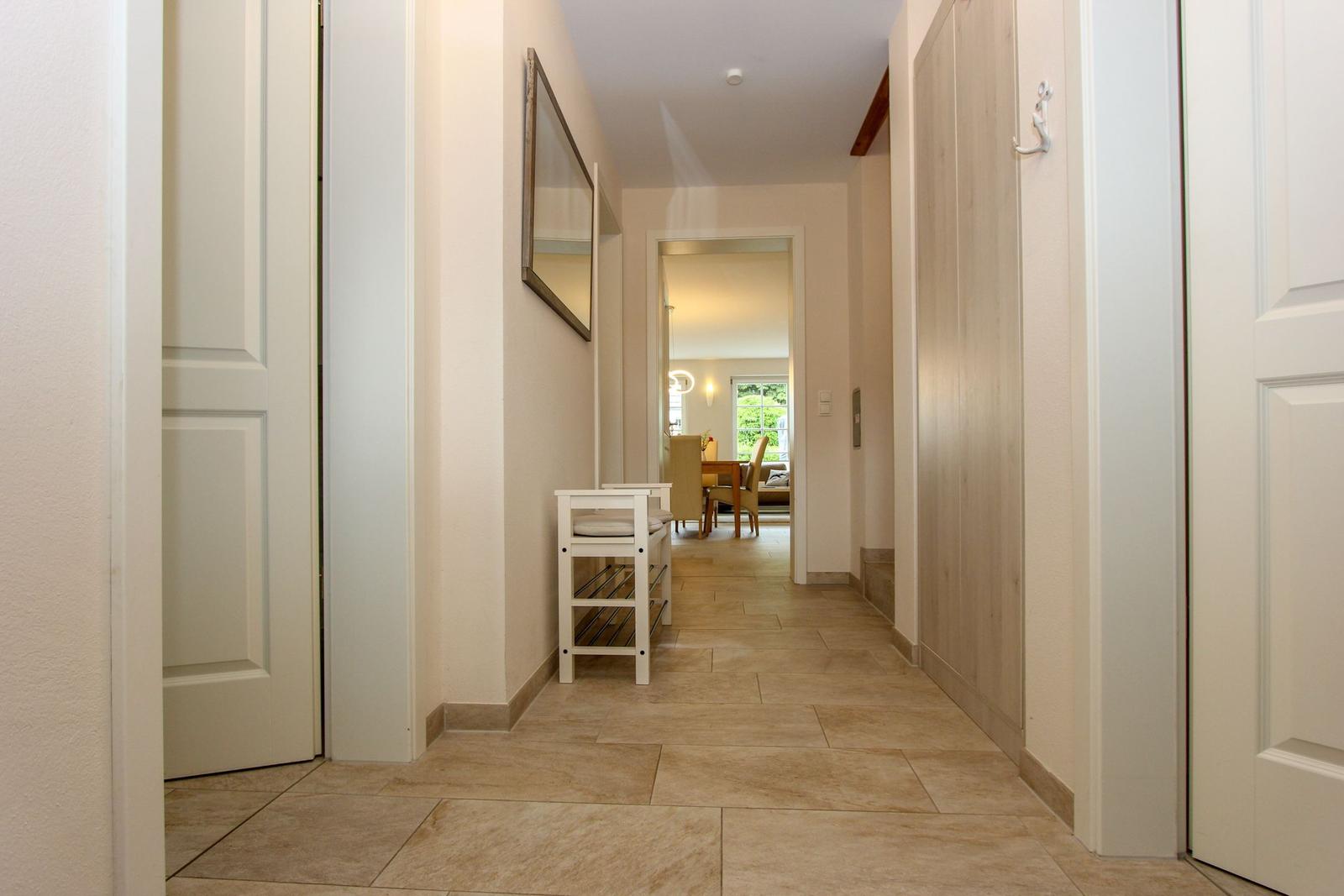 Flur mit Holztüren, Wandspiegel und Schuhschrank. Blick in Esszimmer mit Tisch und Stühlen.