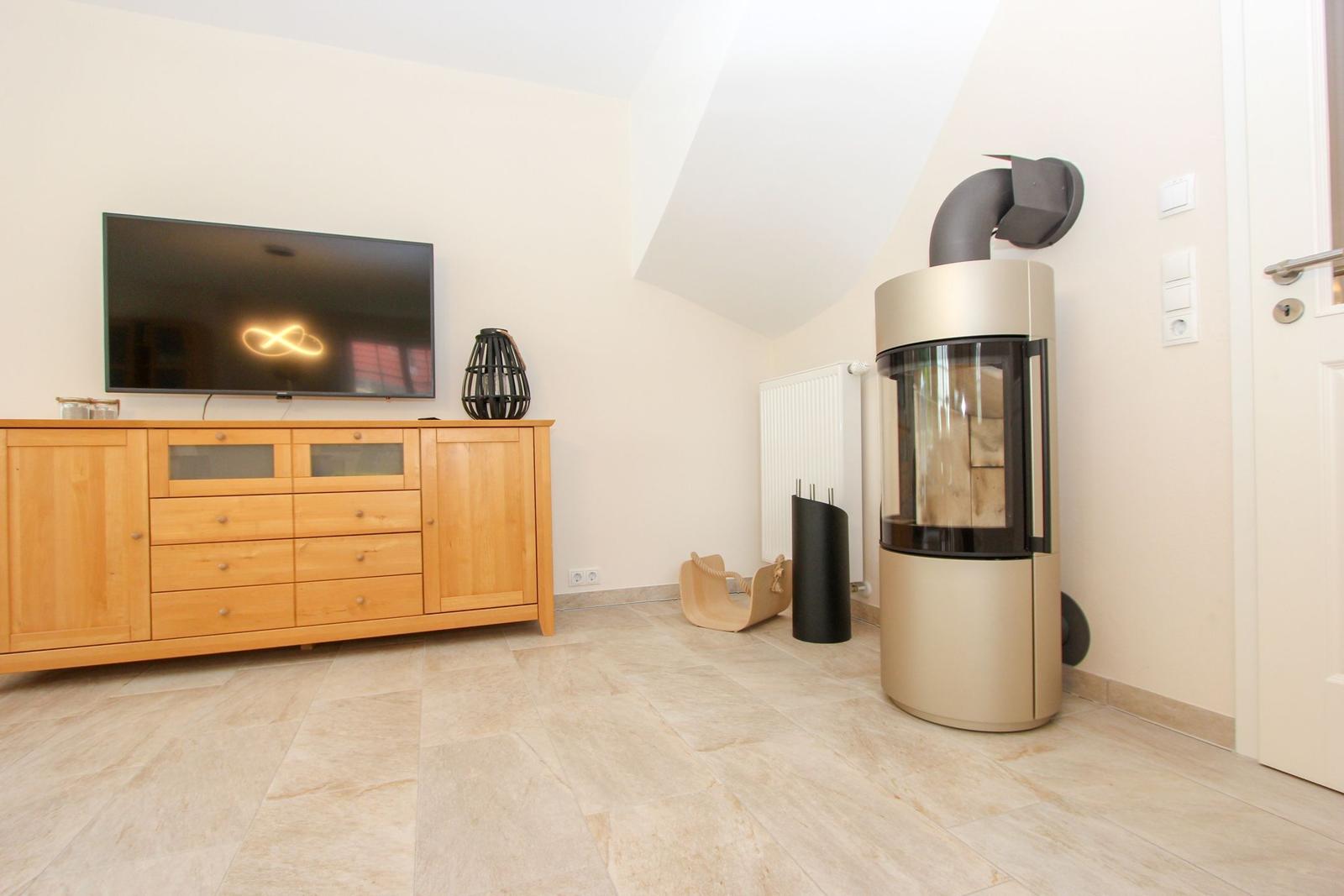 Wohnzimmer mit TV, Holzschrank und Kaminofen an der Wand.