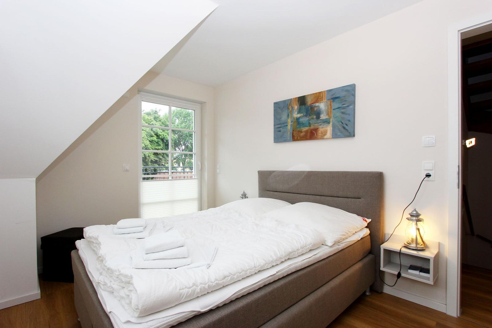 Schlafzimmer mit Bett, Fenster und Wandbild. Nachttisch mit Laterne.