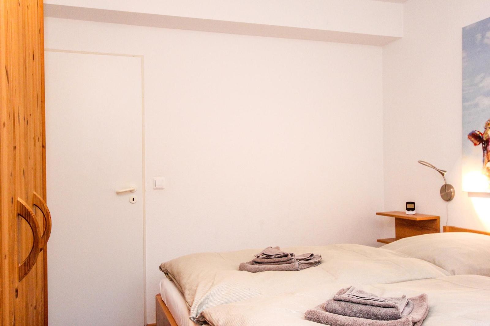 Schlafzimmer mit Bett, Nachttisch und Wandlampe. Holzschrank und Tür sind sichtbar.