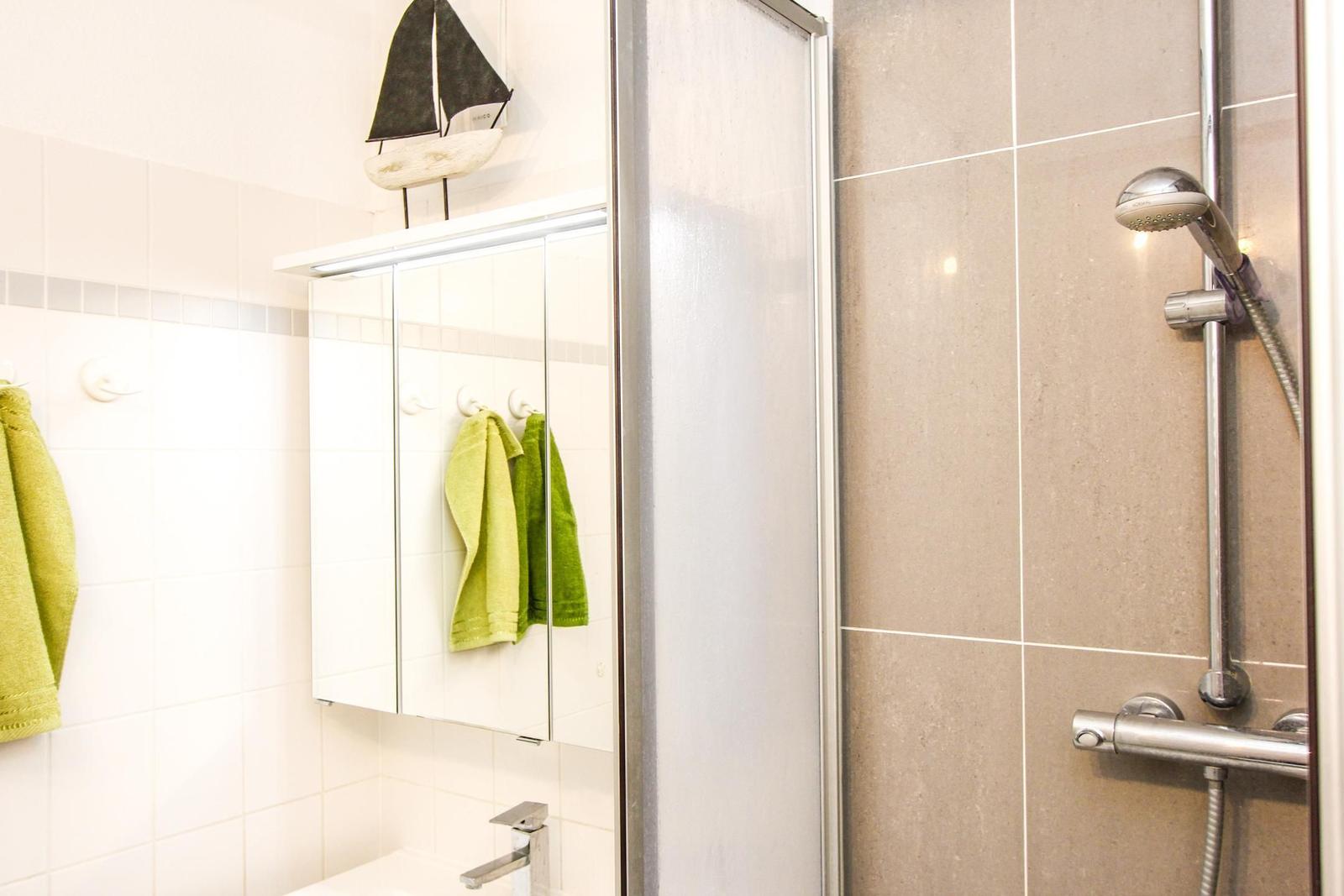 Dusche mit Duschbrause, Spiegelschrank und grünen Handtüchern.
