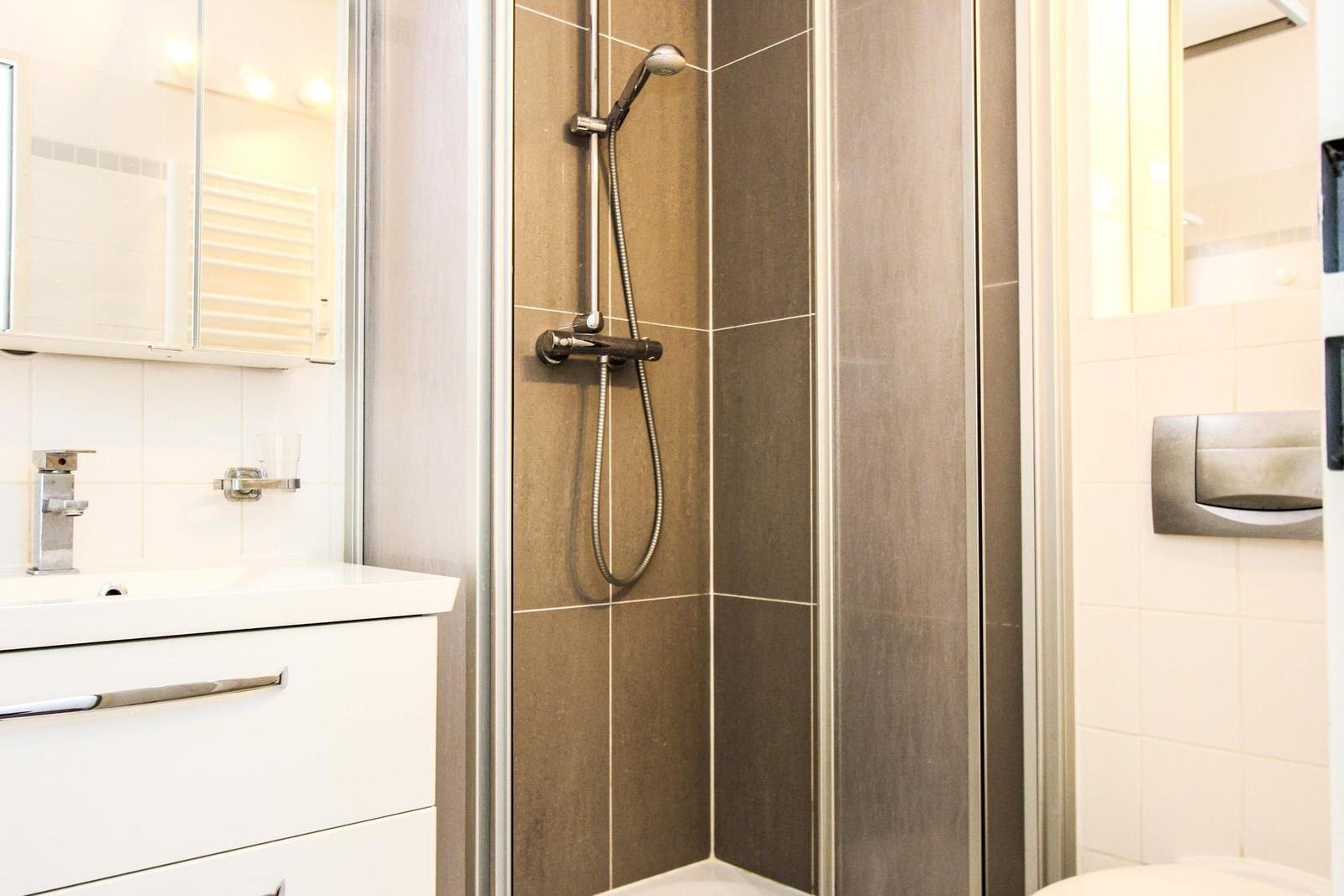 Dusche mit Duschbrause, Waschbecken und Spiegel im Badezimmer.