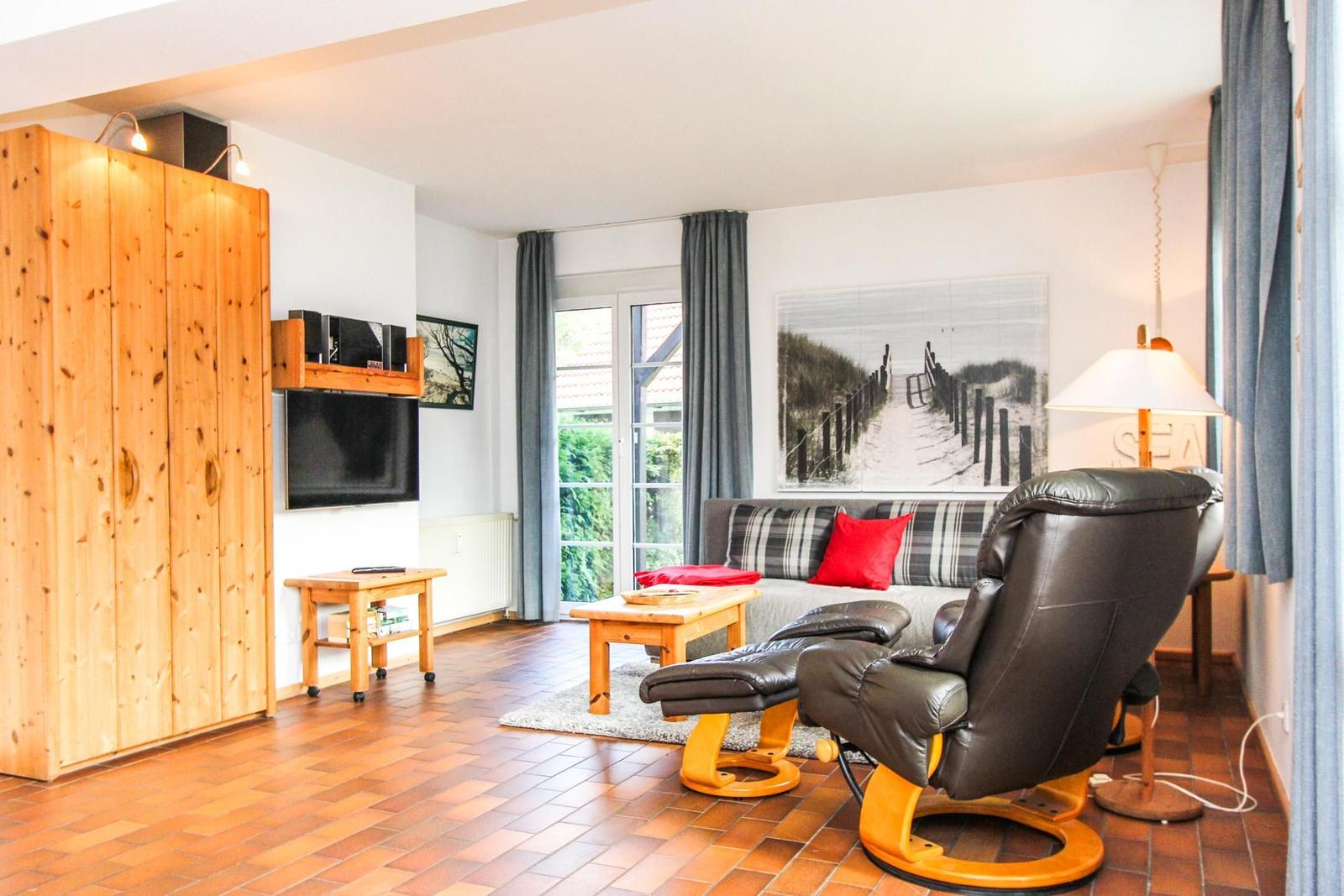 Wohnzimmer mit Sofa, Ledersessel und Holzmöbel. Fenster mit Blick nach draußen.