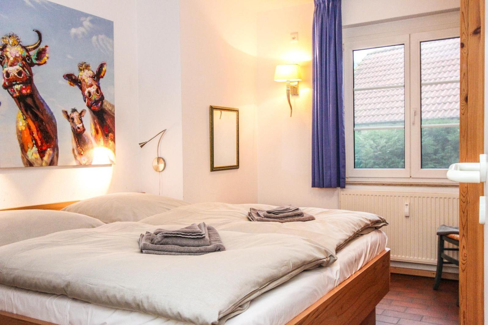 Schlafzimmer mit Bett, Wandbild von Kühen, Fenster und Wandleuchte.