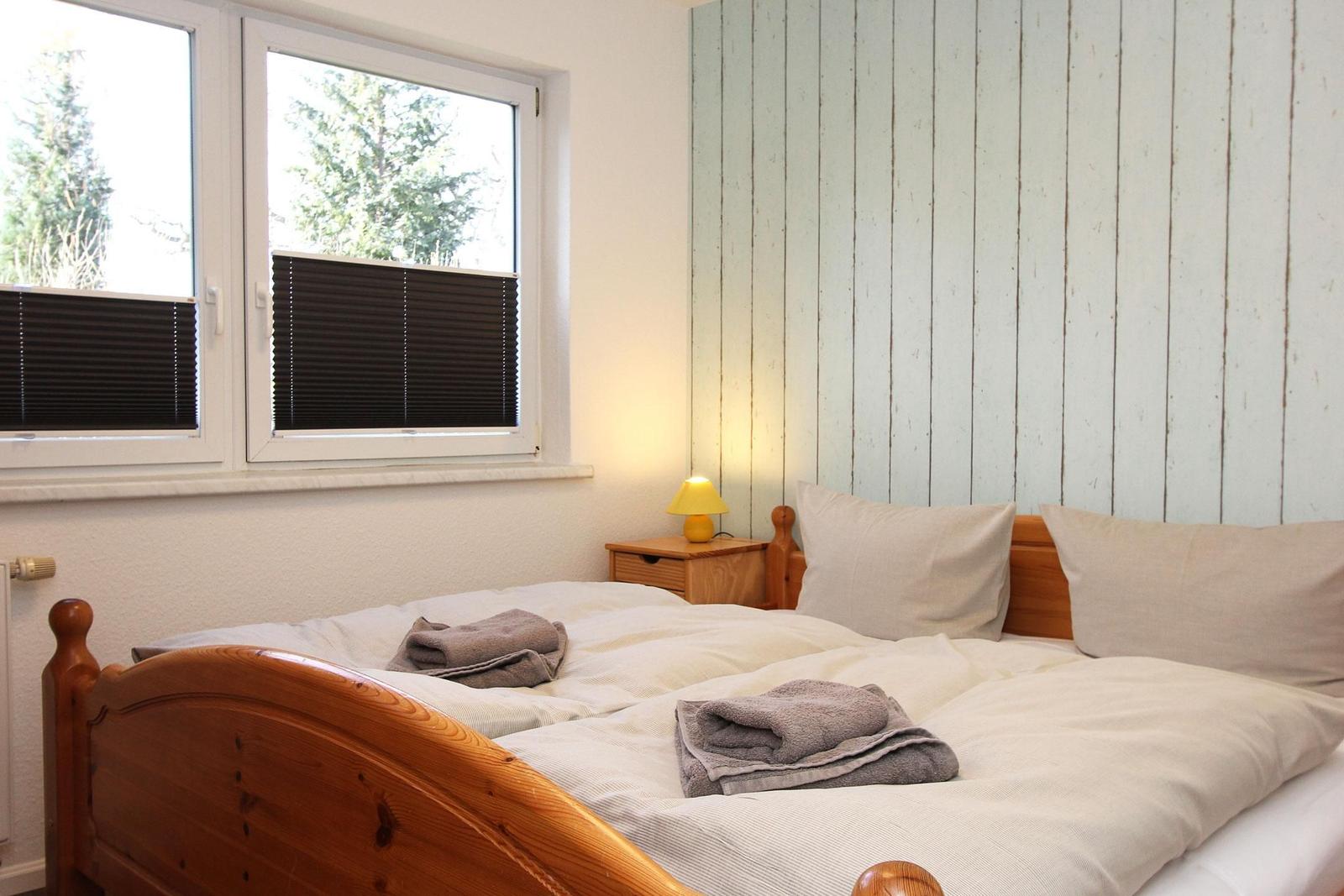 Schlafzimmer mit Holzbett, Fenster und Nachttisch mit Lampe.