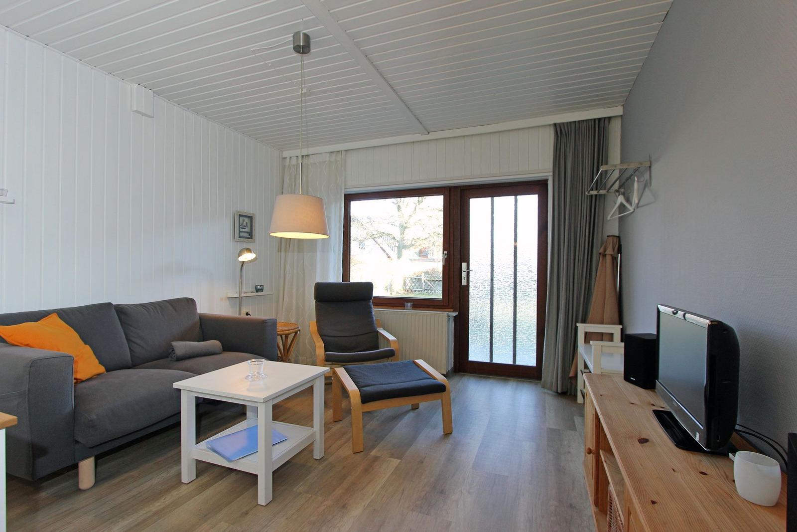 Wohnzimmer mit Sofa, Sessel, Fernseher und Blick auf Wasser.