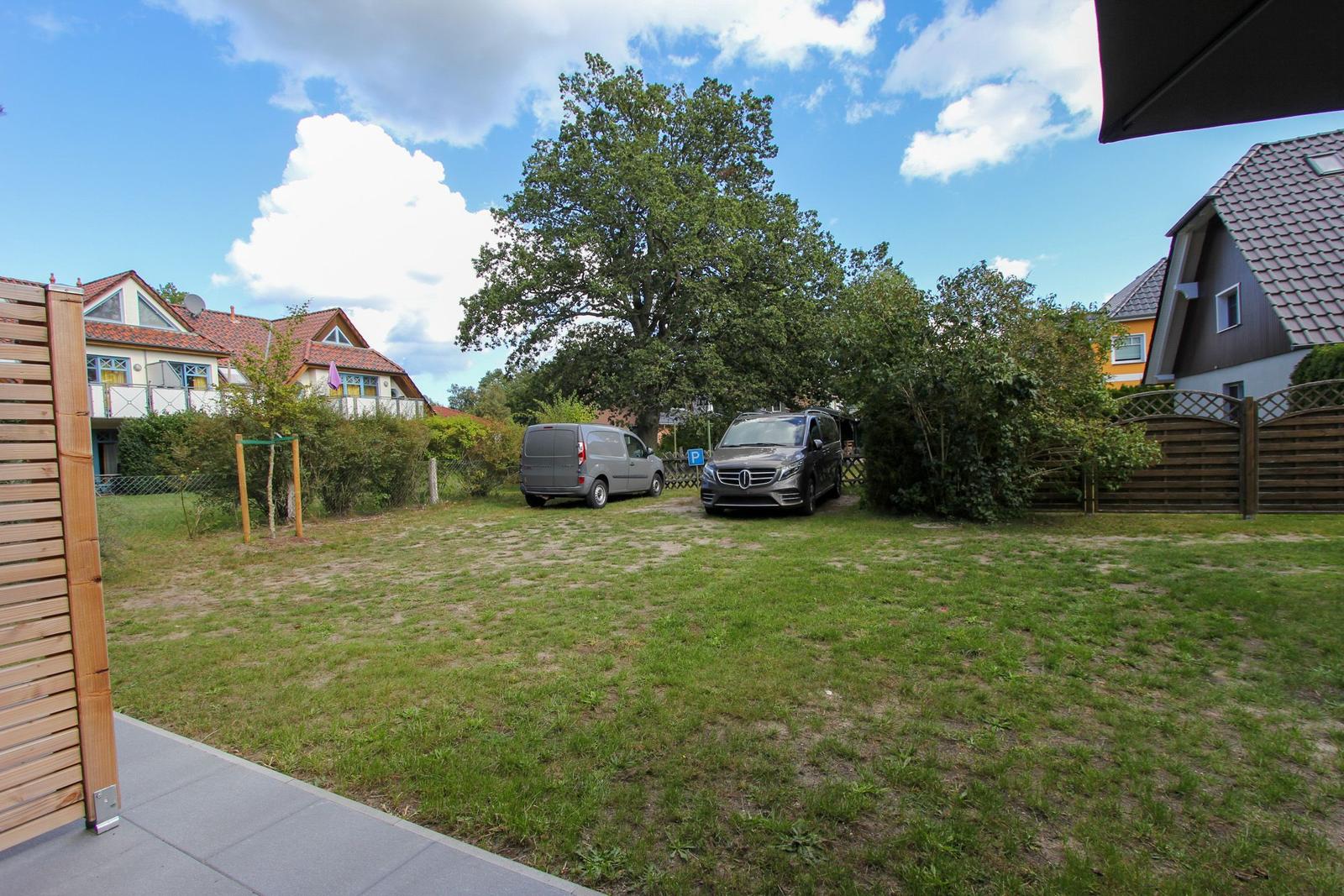 Grüner Garten mit zwei parkenden Autos und einem großen Baum im Hintergrund.