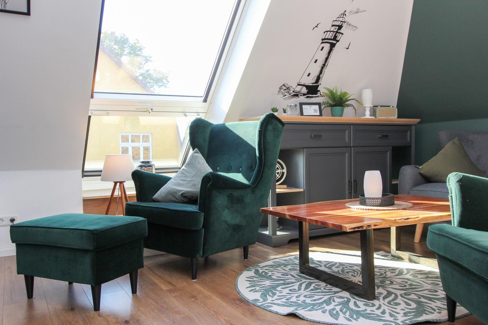Ein Wohnzimmer mit grünem Sessel, Holztisch und Dachfenster.
