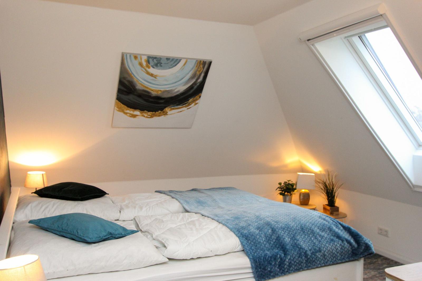 Schlafzimmer mit Dachschräge, Bett, Decke, Nachttische und Fenster.