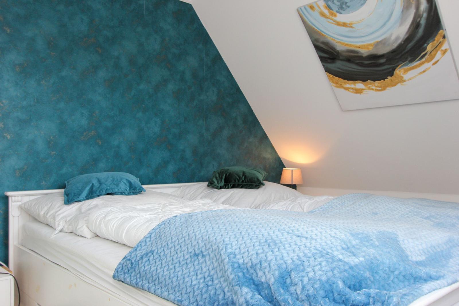 Schlafzimmer mit Bett, blauer Wand und Wandbild.