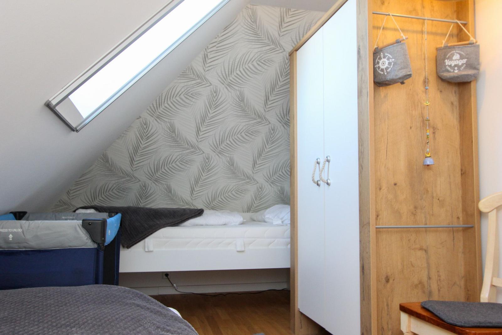 Schlafzimmer mit Dachschrägen, Babybett und Kleiderschrank.