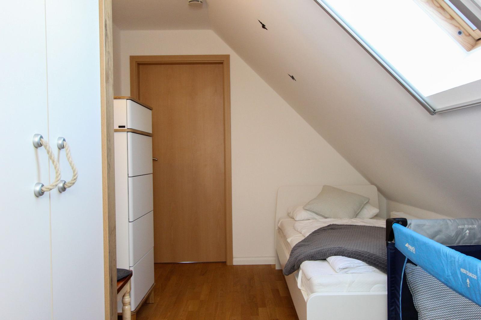 Schlafzimmer mit Dachschrägen, Bett, Kinderbett und Schrank. Dachfenster sorgt für Tageslicht.
