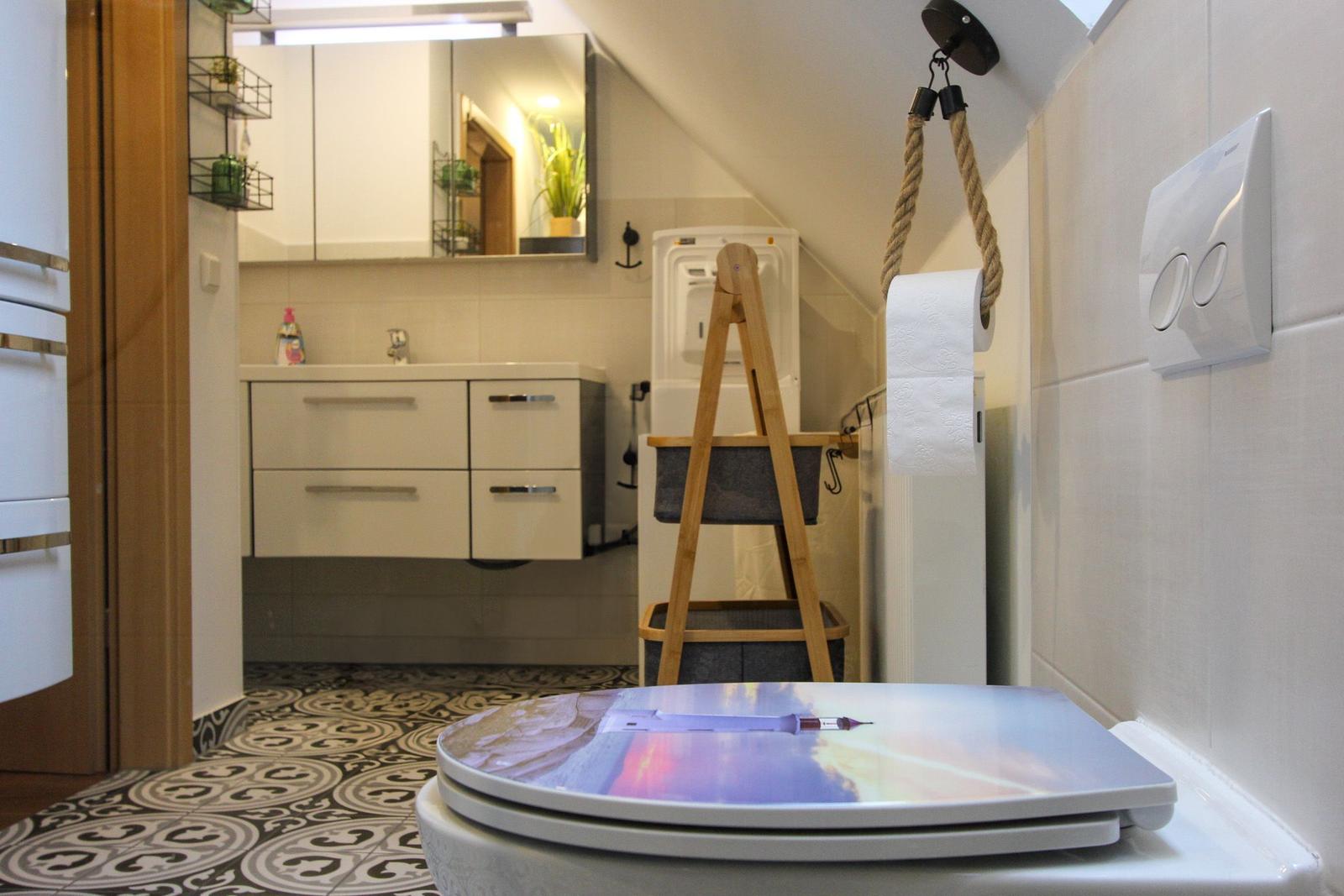 Badezimmer mit Waschbecken, Spiegel und Toilette. Holzregal und Musterboden.