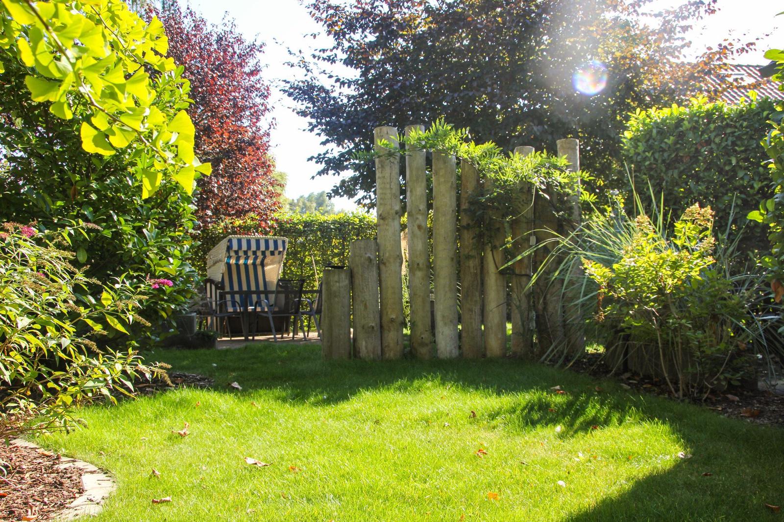Garten mit grünem Rasen, Holzpfostenzaun und Liegestuhl mit Streifenmuster.