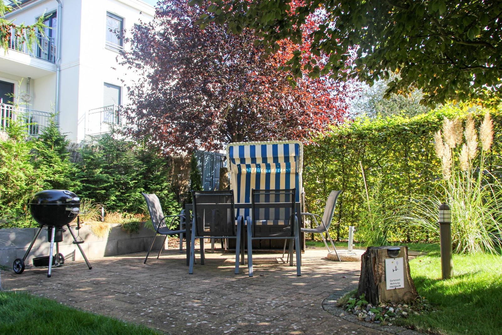 Garten mit Liege, Tisch, Stühlen und Grill. Hinterhof mit Bäumen und Hecke.