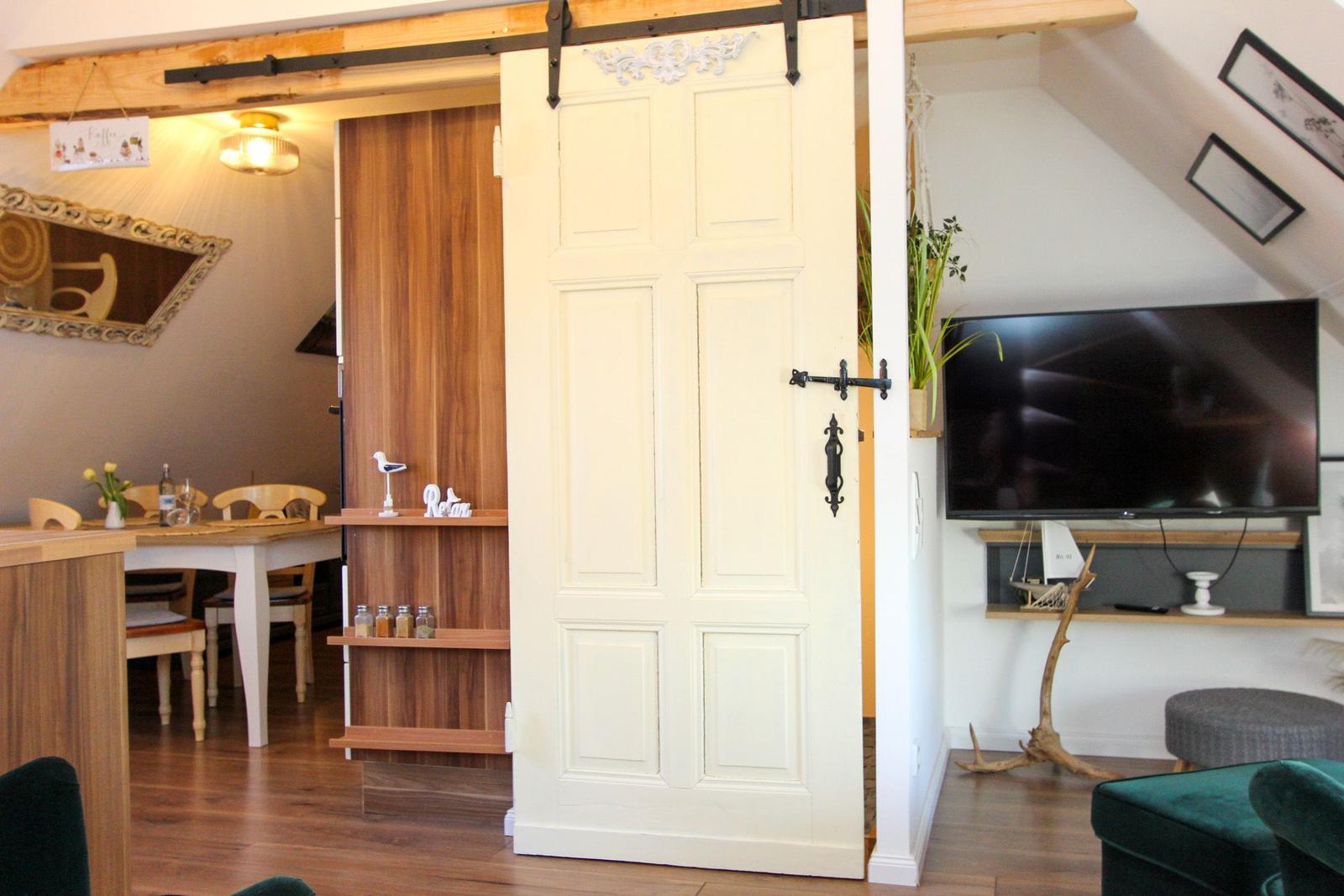 Raum mit Schiebetür, Fernseher und Holzmöbeln. Decke mit Sparren und Wanddekoration.