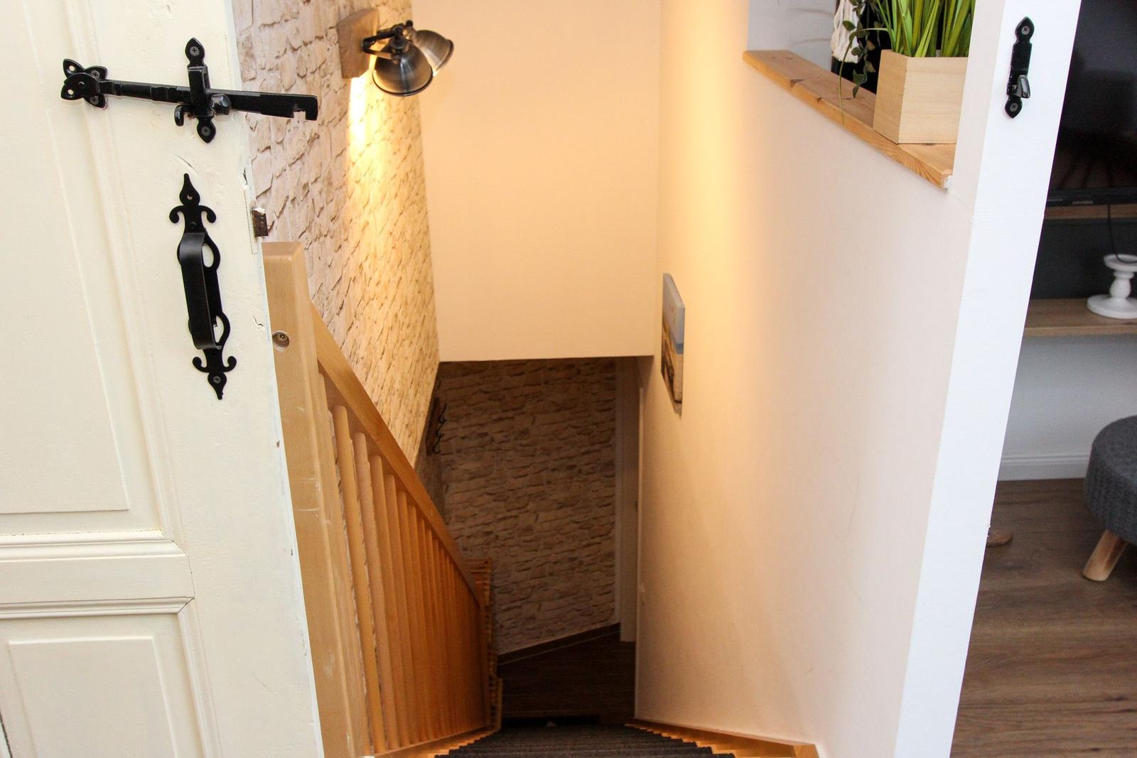 Helle Treppe mit Holzgeländer und Steinwand. Tür mit schwarzen Metallgriffen.